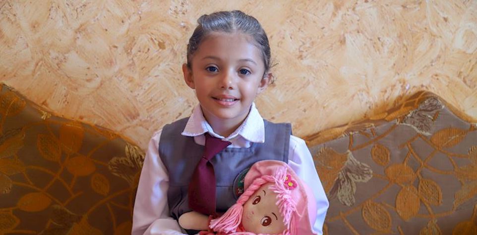 Little school girl holding a doll